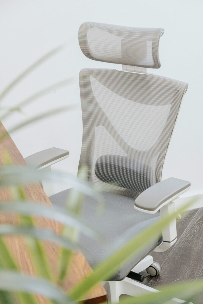 Modern ergonomic office chair with sleek design placed beside a wooden desk, promoting comfort and back support in the workplace.